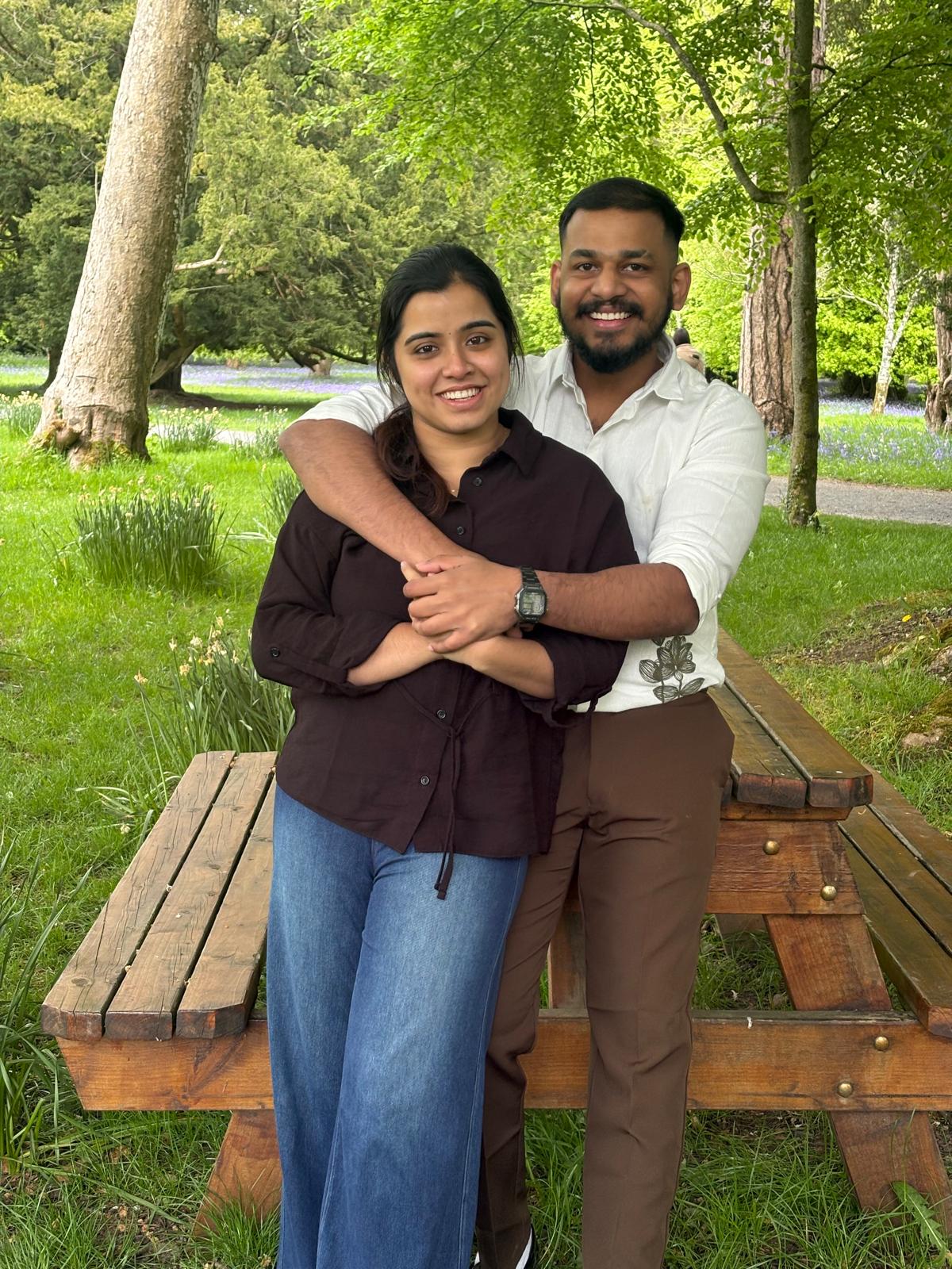 Leyo and Anju smiling together beside a picnic table in a leafy garden.