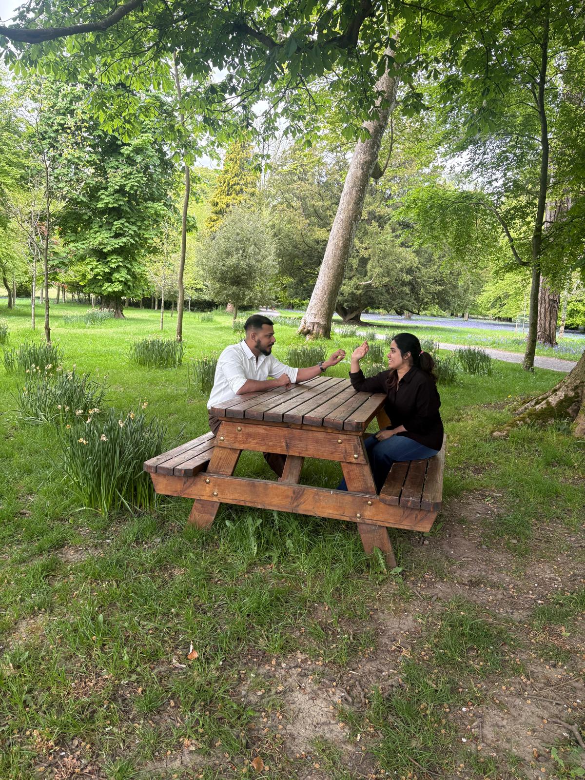 Leyo and Anju sharing a playful moment across a picnic table beneath the trees.