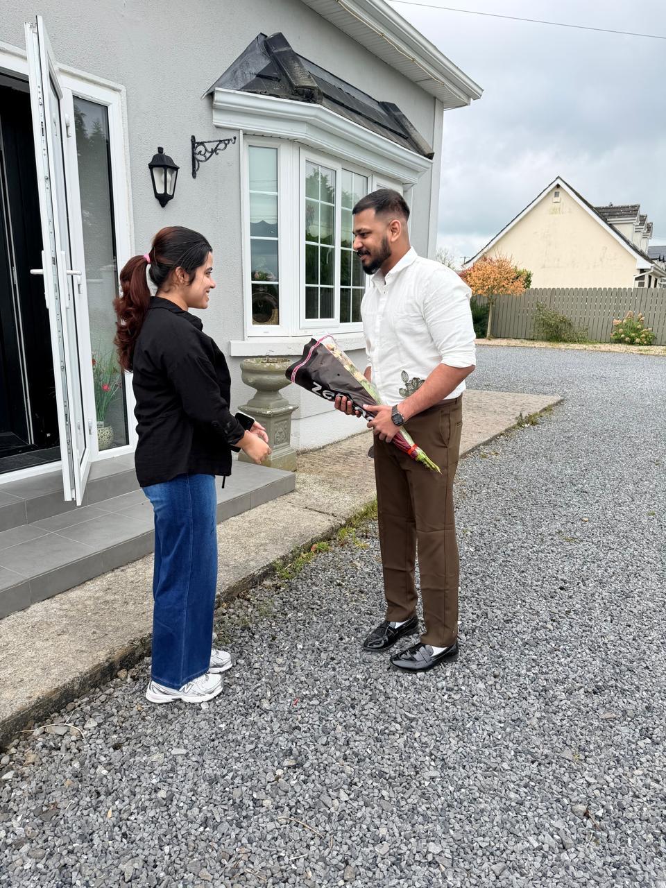 Leyo holding a bouquet as he and Anju smile at each other outside a house.