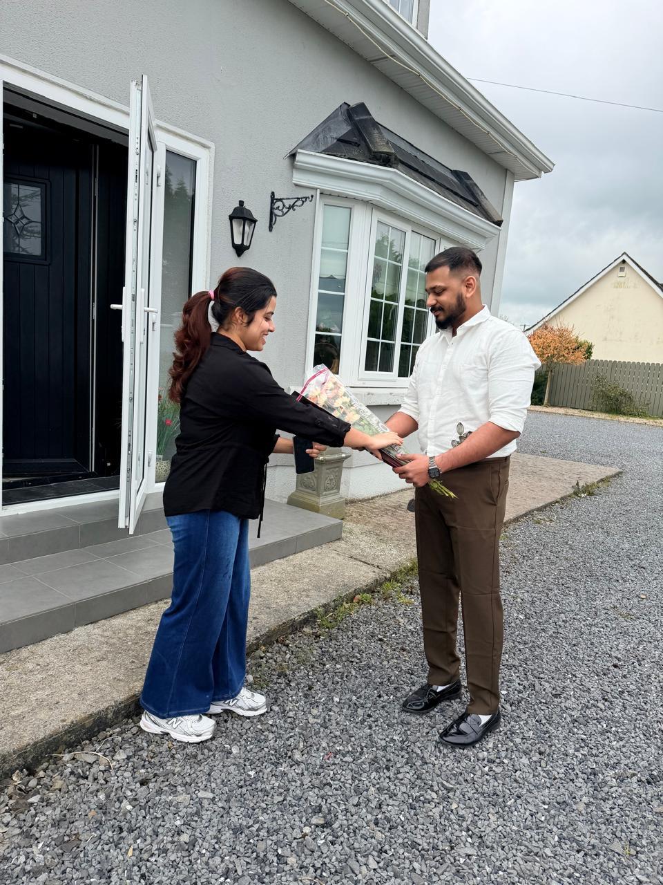 Anju reaching to accept the bouquet from Leyo at the front door.